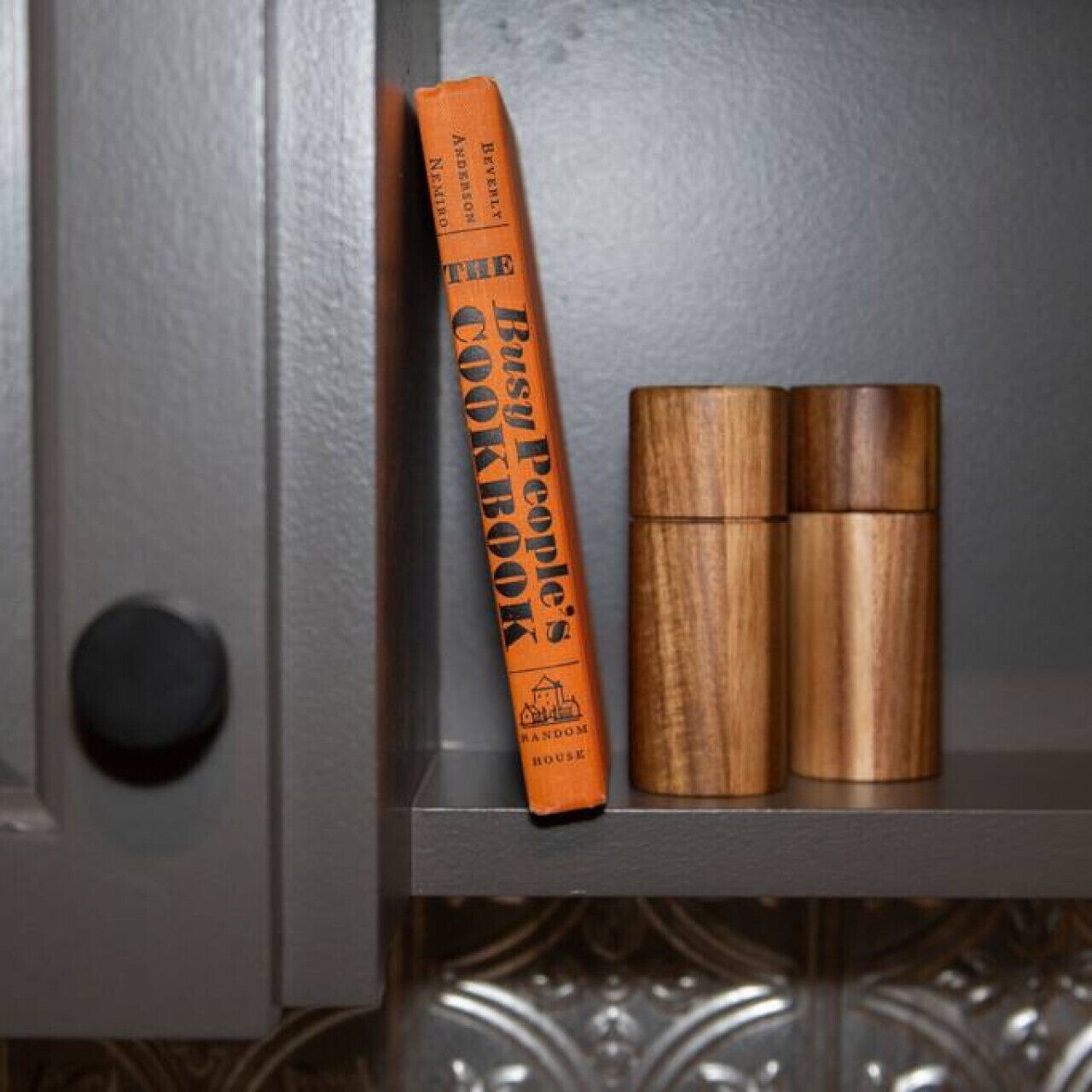 A kitchen shelf with a cookbook and two wooden containers.