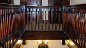 Un imposant escalier en bois, surmonté d’un grand lustre central, et flanqué de deux portes portant les numéros 301 et 302.