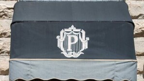 L’entrée d’un hôtel, avec un auvent sombre, une grande porte vitrée et une façade en pierre.