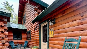 A wooden cabin with a porch, two rocking chairs, and a caution sign for falling ice and snow. - Luxury Log Cabin • Paradise in the Lakes Region (Naples)