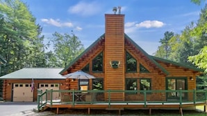 A wooden cabin with a steeply pitched roof, a chimney, and a porch with a green railing. - Luxury Log Cabin • Paradise in the Lakes Region (Naples)