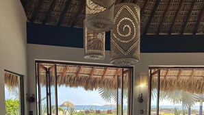 A dining area with a glass table, wooden chairs, and a view of the ocean. - Villa De Las Rocas- Luxury Rental, Puerto Escondido, Villa de las Rocas - Luxury Rental, Puerto Esco (Puerto Escondido)