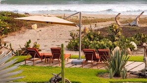 A beachside patio with lounge chairs and a table, overlooking the ocean. - Villa De Las Rocas- Luxury Rental, Puerto Escondido, Villa de las Rocas - Luxury Rental, Puerto Esco (Puerto Escondido)