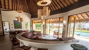 A modern living area with a curved sofa, wooden stools, and a large vase. - Villa De Las Rocas- Luxury Rental, Puerto Escondido, Villa de las Rocas - Luxury Rental, Puerto Esco (Puerto Escondido)