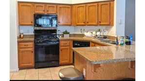 Una cucina con mobili in legno, un piano cottura nero e un ripiano in granito.
