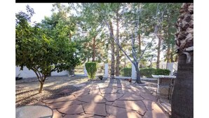 Un patio lastricato con piastrelle in pietra, circondato da alberi e un recinto bianco.