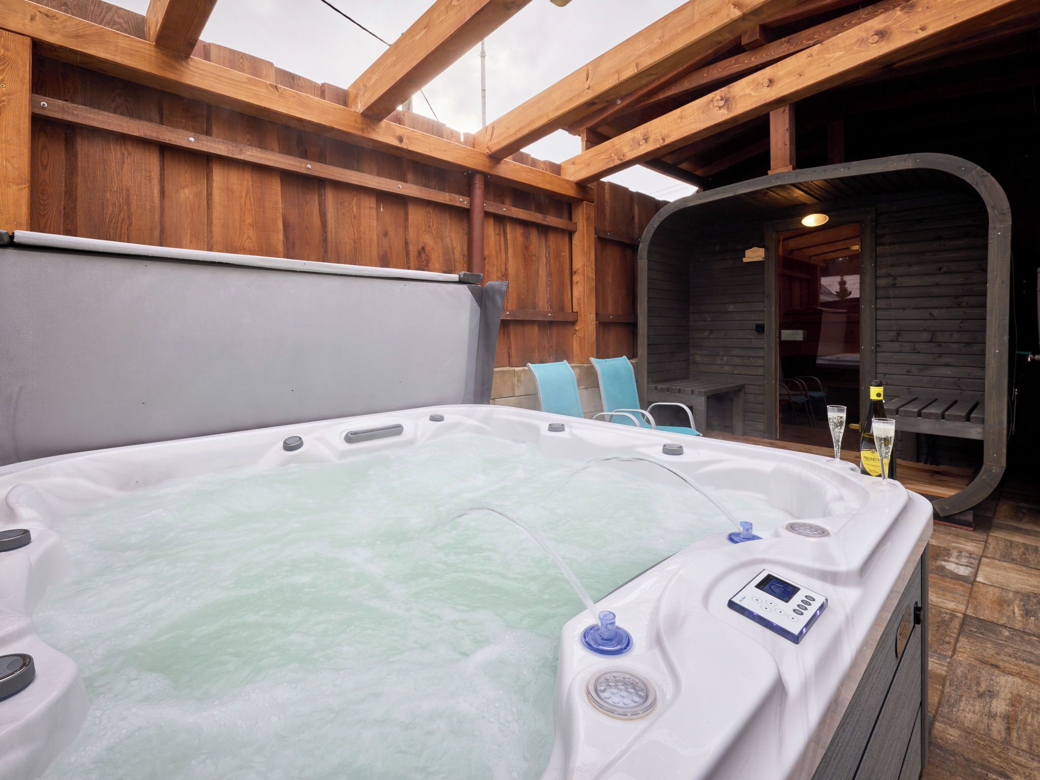 A hot tub with a control panel, two chairs, and a bottle of wine.
