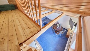 Et soveværelse i træ med skråvægge, en trætrappe, et lille spiseområde og en grøn sofa.