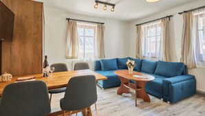 A modern living room with a wooden dining table, blue sofa, and a small round coffee table. - Marika 1 by Interhome (Cerny Dul)