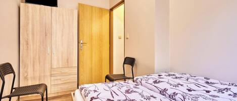A bedroom with a bed, two chairs, a wardrobe, and a door.