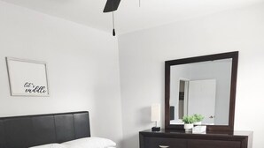 Et soveværelse med seng, kommode, spejl og loftventilator.