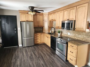 A kitchen with wooden cabinets, stainless steel appliances, a granite countertop, and a ceiling fan.