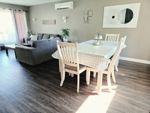A dining area with a table set for four, a grey sofa, and a dark wooden floor. - Modern 3BR Upstairs Suite | Private Entrance | Sault Ste. Marie (Sault Ste. Marie)
