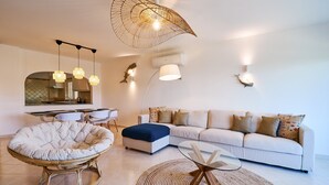 A modern living room with a white sofa, a round wicker chair, a glass coffee table, and a unique ceiling light fixture. - Apartment Delphine with pool (Porches)