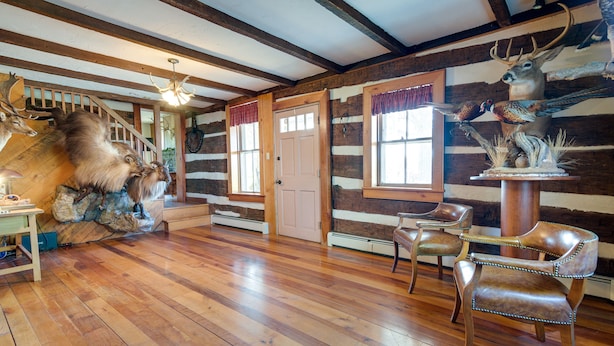 A log cabin interior with wooden floors, a staircase, and rustic decor including mounted animal heads. - Rustic Wellsville Home - 5 Mi to Roundtop Mountain (Wellsville)