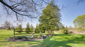 A well-maintained garden with a wooden bench, a stone sculpture, and a variety of trees. - Rustic Wellsville Home - 5 Mi to Roundtop Mountain (Wellsville)