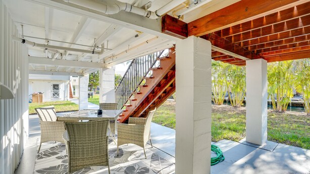 Un patio techado al aire libre con mobiliario de mimbre, suelo de hormigón y una escalera de madera.