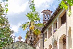 A building with a stone wall, palm trees, and a bell tower. - Casa Cassettari Apartment With Garden (Coreglia Antelminelli)