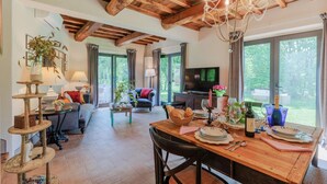 A spacious living room with a wooden dining table set for a meal, a television, and a large window offering a view of the outdoors.