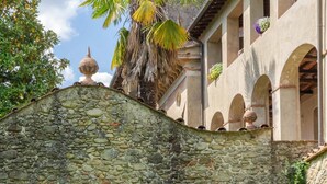 A stone archway leading to a building with a bell tower, surrounded by greenery and palm trees.