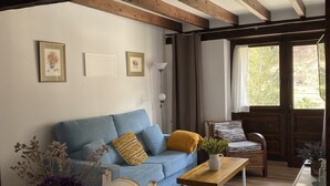 Un soggiorno con un divano blu, travi in legno, un tavolo da pranzo con sedie e vista attraverso una porta vetrata.