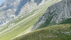 Un piccolo edificio in pietra con tetto rosso, immerso in una valle erbosa, circondato da montagne impervie.
