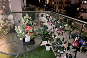 A balcony with a glass table, potted plants, and hanging light fixtures.