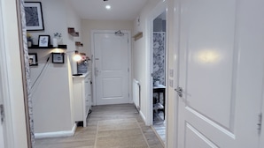 Een smalle gang met een witte deur aan het einde, een radiator op de muur en een kamerbreed tapijt met een patroon op de vloer.