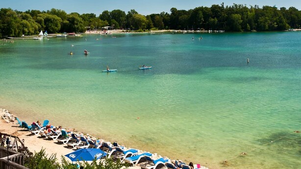 A beach with clear turquoise water, people kayaking, and beach chairs lined up along the shore.