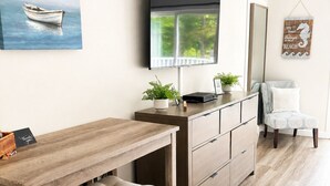 A modern kitchen with a wooden table, bar stools, a flat-screen TV, and a painting of a boat.