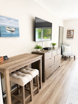 Una cocina moderna con una mesa de madera, taburetes de bar, un televisor de pantalla plana y un cuadro de un barco.