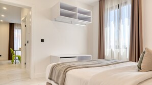 A modern bedroom with a large bed, a white wardrobe, a built-in shelf, and a view of a dining area.