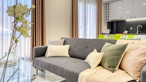 A modern living room with a grey sofa, a glass coffee table, and a vase with white flowers.
