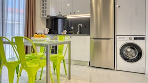 A modern kitchen with stainless steel appliances, a glass table, and bright green chairs.