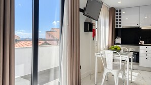 A modern kitchen with white cabinets, a flat-screen TV mounted above the counter, and a dining area with a glass table and white chairs. - Beco Santa Emilia 4Q, a Home in Madeira (Funchal)