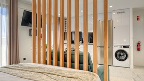 A hotel room with a bed, a washing machine, a TV, and a kitchen area visible through a partition. - Beco Santa Emilia 4Q, a Home in Madeira (Funchal)