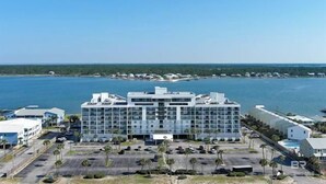 A modern hotel with a central atrium, multiple floors, and a parking lot with palm trees. - Lagoon Front w/Boat Launch & Parking~2BR/1B (Gulf Shores)