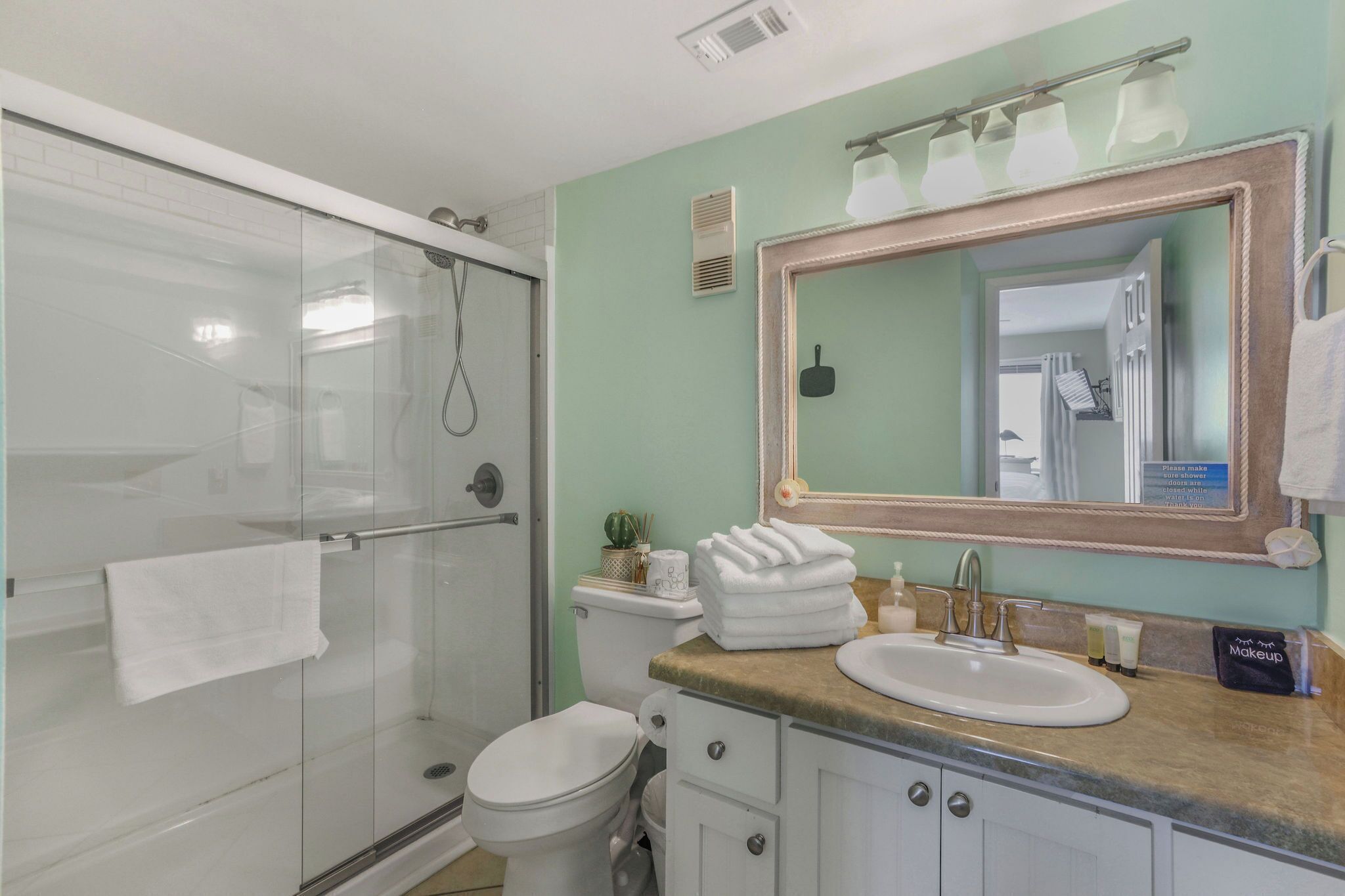 Een badkamer met een douchecabine van glas, een wit toilet, een wastafel met een kastje en een grote spiegel.