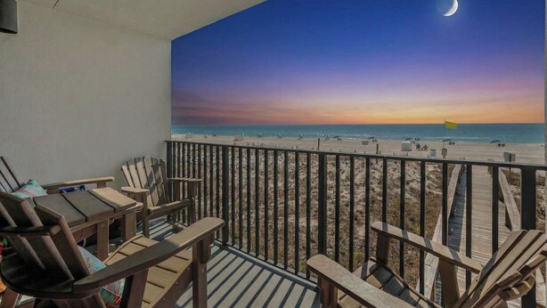 Een balkon met houten stoelen en uitzicht op het strand bij zonsondergang.