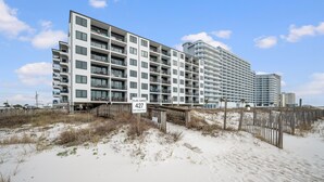Een strandhotel met meerdere verdiepingen, een zandstrand ervoor en een houten omheining.