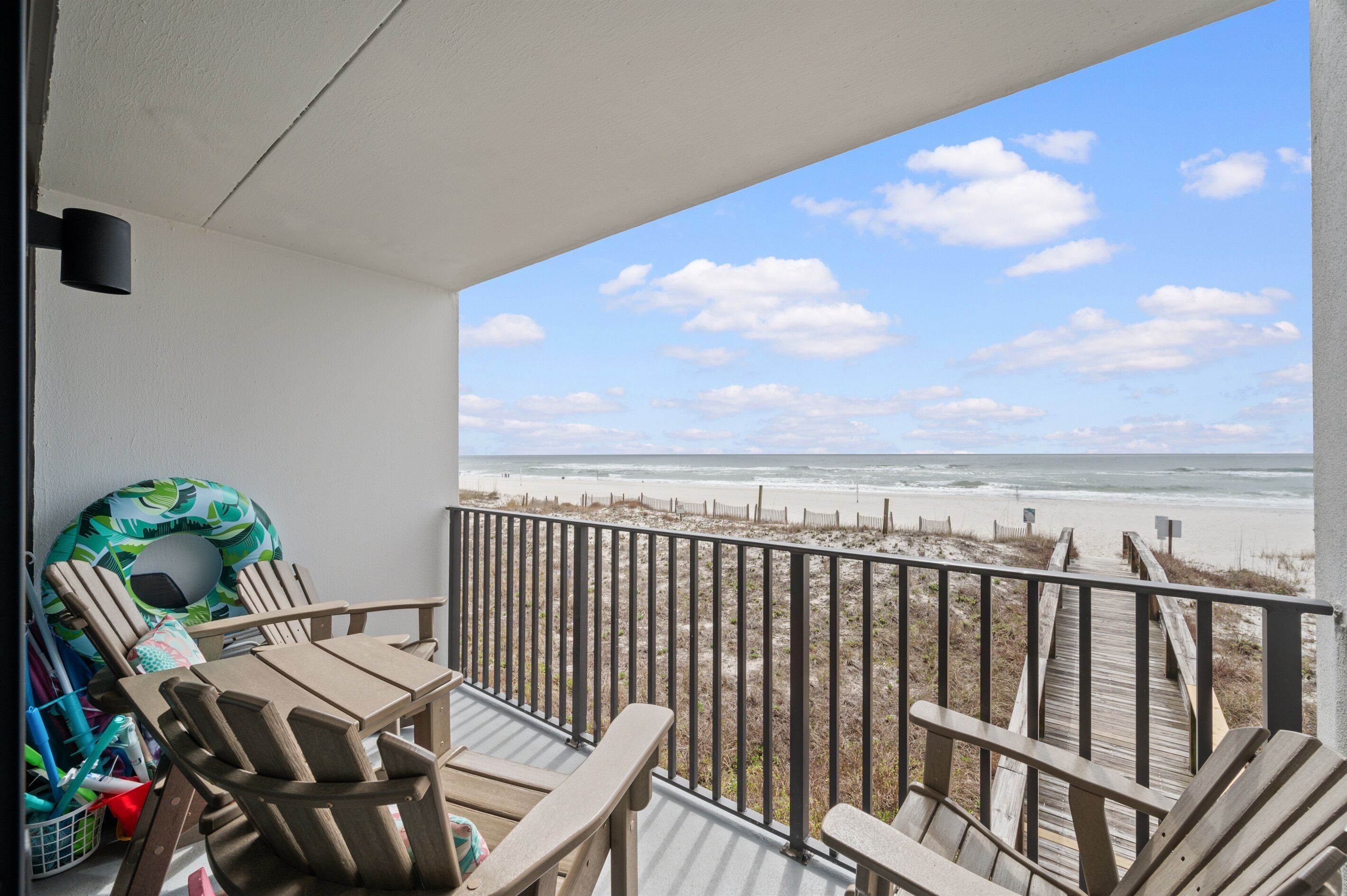 Un balcon avec vue sur la plage, des chaises en bois, un flotteur pour la piscine et une terrasse en bois.