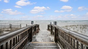 Een houten looppad dat naar een strand leidt, met een heldere lucht en wolken.