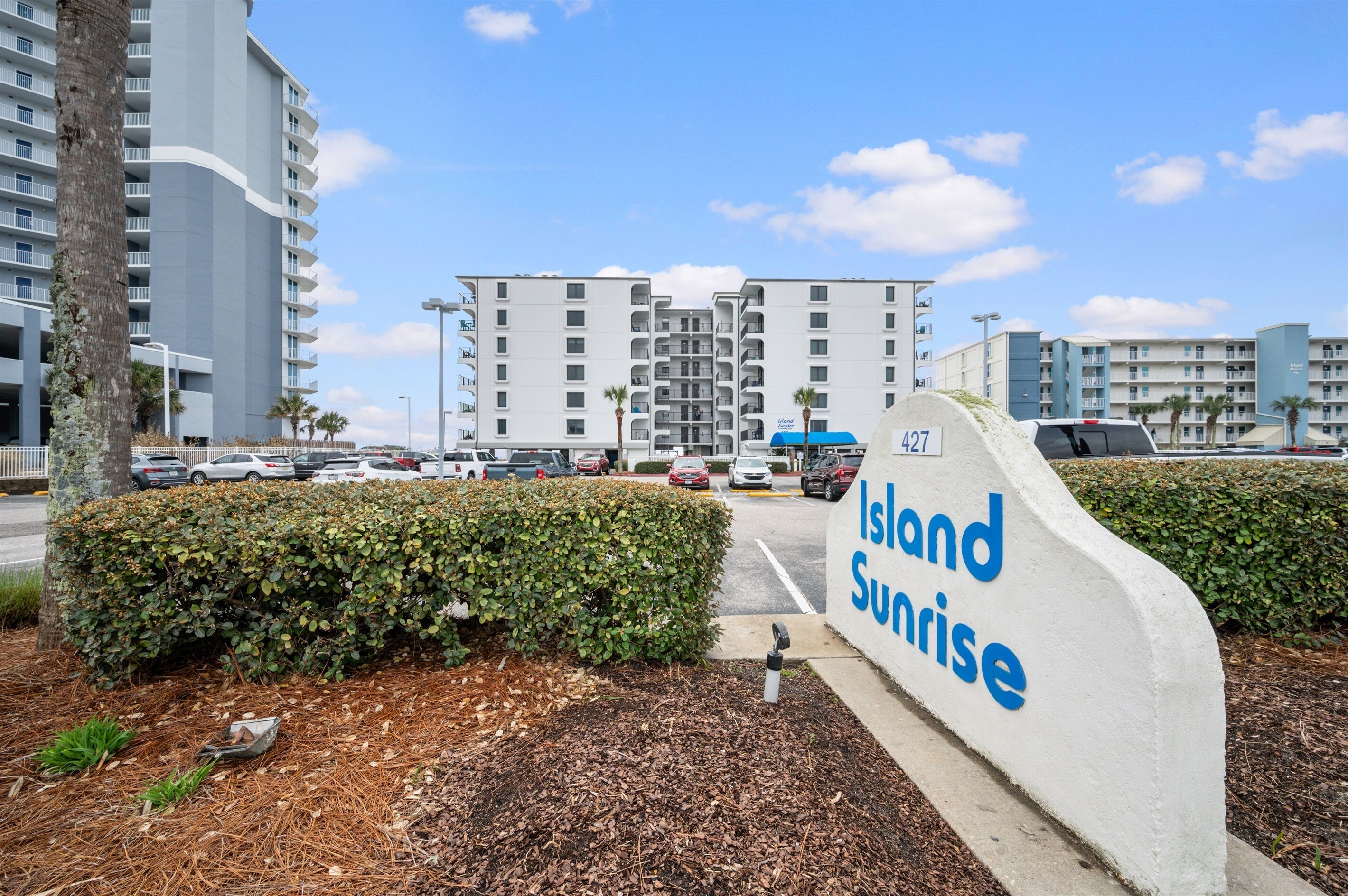 Naamplaatje voor Island Sunrise, met uitzicht op moderne gebouwen en geparkeerde auto's.