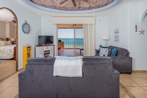 Ein Wohnzimmer mit grauem Sofa, einem Fernseher und einem Balkon mit Meerblick.