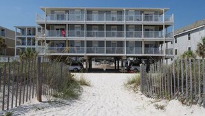 Ett hotell vid stranden med en byggnad i flera våningar, en sandstrand framför och ett trästaket.