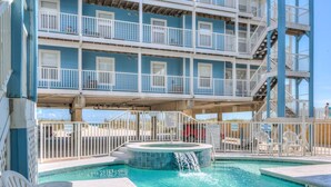 A swimming pool with a hot tub, surrounded by white chairs and a multi-story building with balconies. - Beachside w/Heated Pool~2BR/1B! (Gulf Shores)