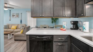 A modern kitchen with dark cabinets, a dishwasher, and a coffee maker. - Beachside w/Heated Pool~2BR/1B! (Gulf Shores)