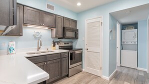 A kitchen with dark cabinets, a white countertop, a stainless steel stove, a microwave, and a built-in oven. - Beachside w/Heated Pool~2BR/1B! (Gulf Shores)