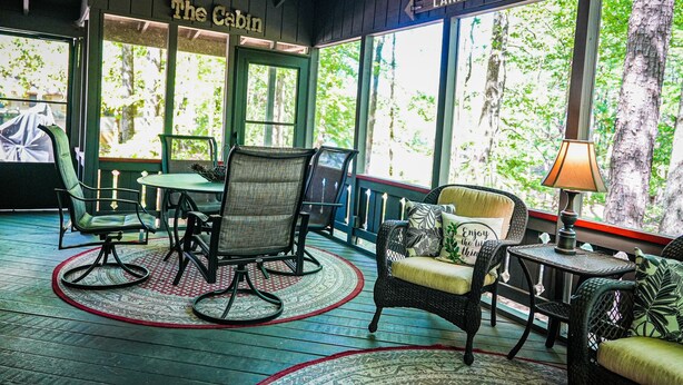 Un intérieur de chalet chaleureux avec un coin repas, des meubles en osier et de grandes fenêtres offrant une vue sur les arbres.