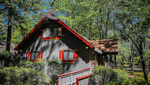 Une cabane avec un toit rouge, des boiseries blanches et une terrasse en bois.